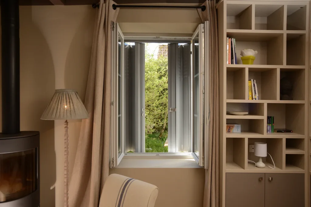 Jalousie aluminium grise sur mesure vue depuis l'intérieur d'un salon, vantaux entrouverts