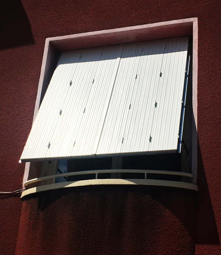 Persienne bois repliable laquée blanc sur mesure, ouverte en projection, façade enduite rouge