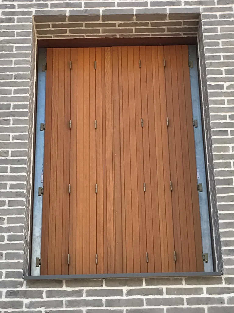 Persienne bois repliable lasurée ton chêne sur mesure, fermée, façade en briques grises