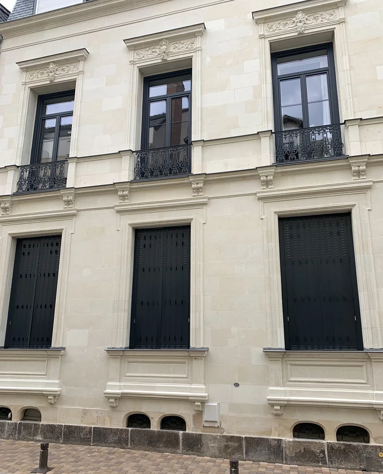 Persiennes fer repliables gris anthracite sur mesure, fermées, façade en pierre de taille avec balcons en fer forgé