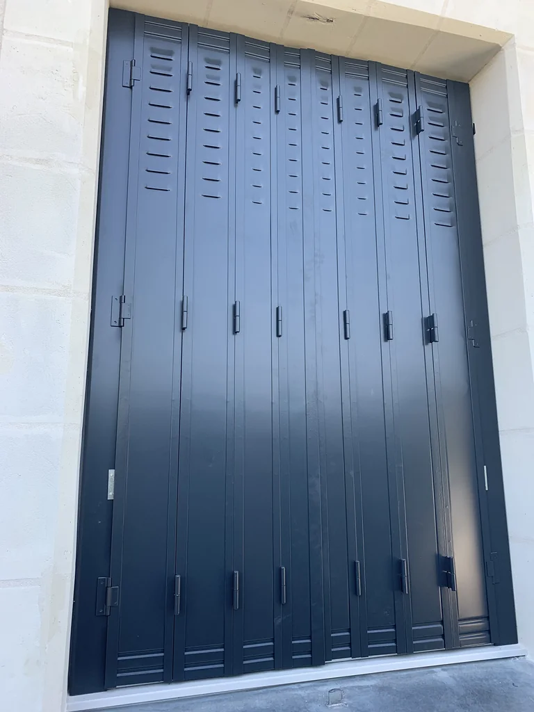 Persienne fer repliable gris anthracite sur mesure à lames ajourées, vue de près dans son tableau en pierre
