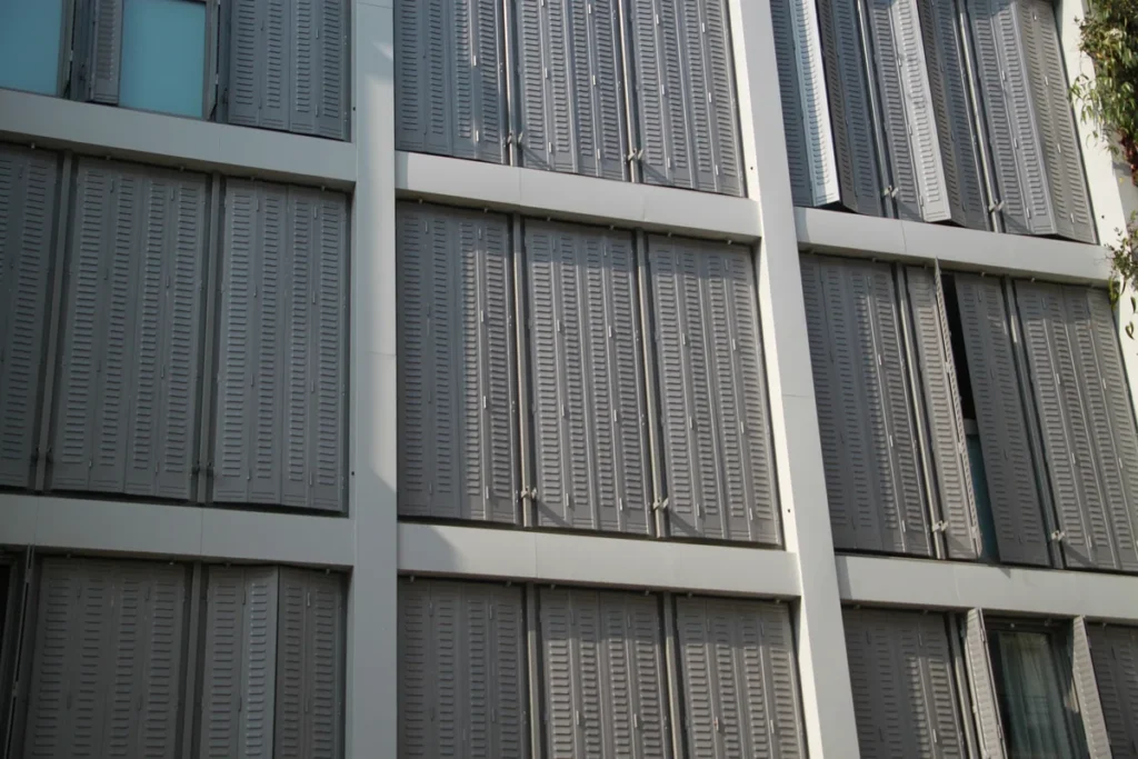 Persiennes fer repliables grises sur mesure sur toute la façade d'un immeuble contemporain