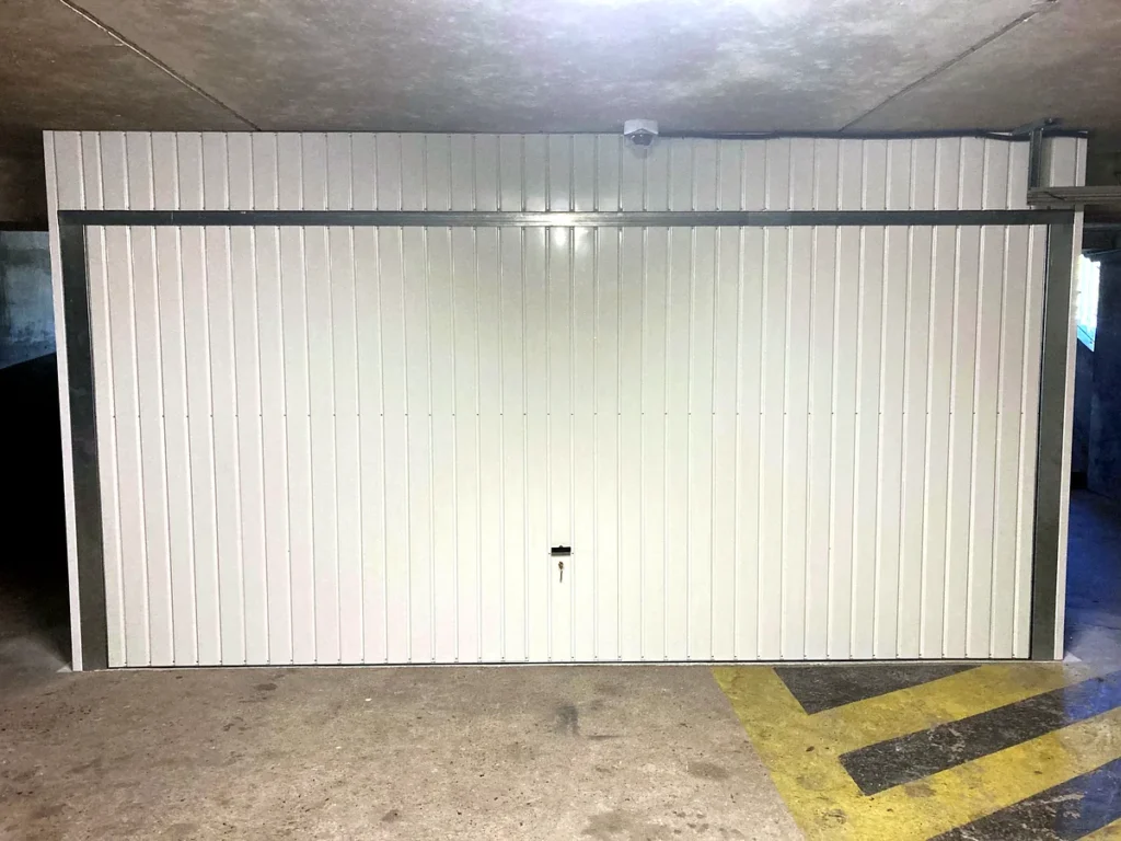 Porte de garage basculante blanche sur mesure avec imposte en tôle au-dessus, vue de face, parking souterrain — photo de réalisation client (Montigny-lès-Cormeilles, Val-d'Oise)