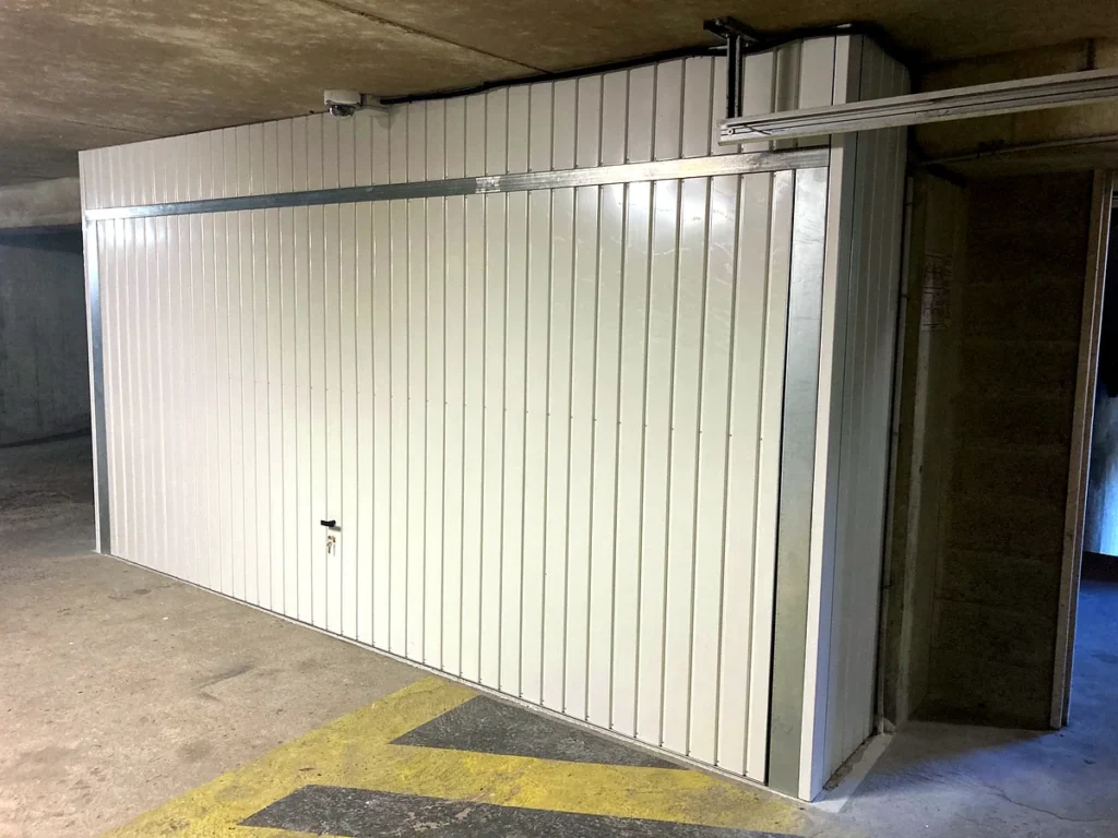 Porte de garage basculante blanche sur mesure avec impostes en tôle au-dessus et sur le côté, vue de l'autre côté, parking souterrain — photo de réalisation client (Montigny-lès-Cormeilles, Val-d'Oise)