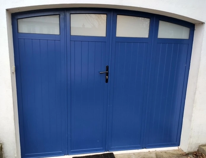 Porte de garage battante aluminium bleue 4 vantaux cintrée à vitrages en partie haute sur mesure, façade enduite blanche