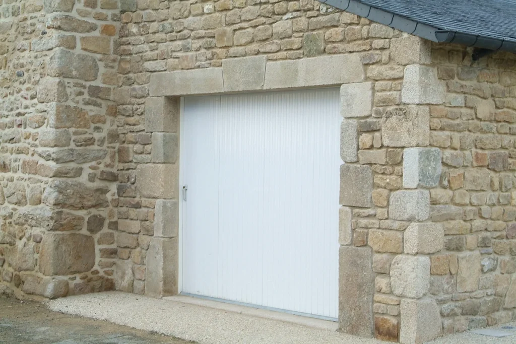 Porte de garage coulissante PVC blanc à lames verticales sur mesure, maison en pierre