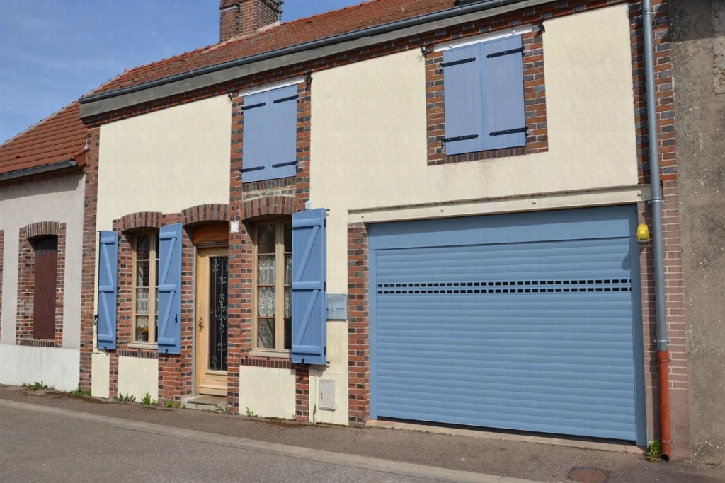 Porte de garage enroulable aluminium bleue à rangée de hublots sur mesure, maison en briques aux volets assortis