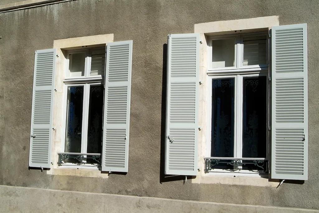 Volets battants bois gris clair persiennés sur mesure, façade ancienne avec appuis en fer forgé