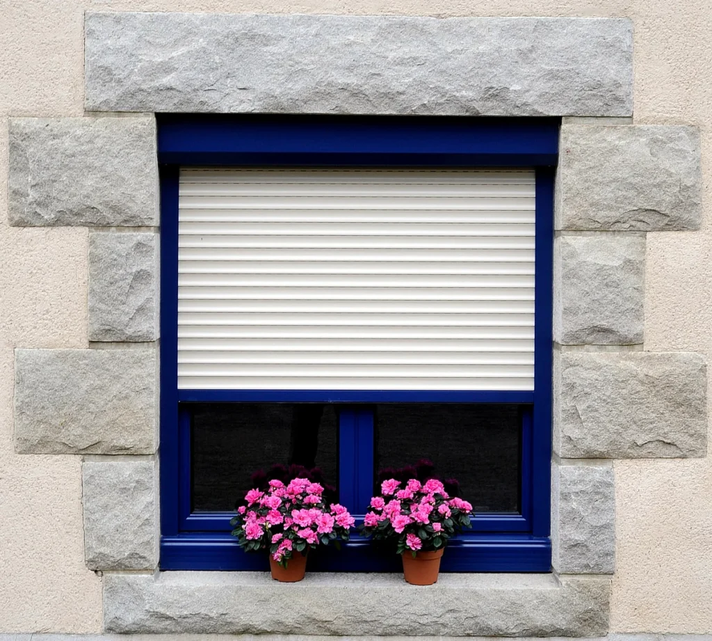 Volet roulant aluminium blanc à coffre bleu sur mesure, fenêtre fleurie à encadrement de granit